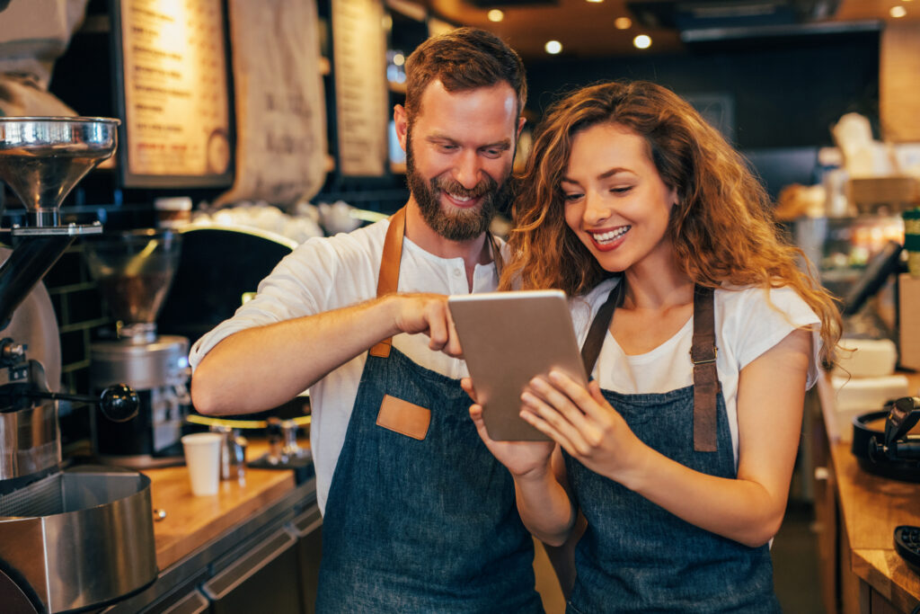 Zwei Café-Mitarbeiter in Schürzen nutzen ein Tablet, um Arbeitszeiten digital zu verwalten.