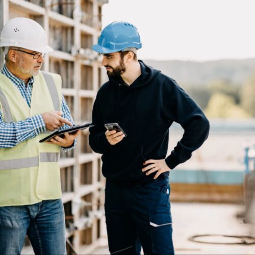 Bauleiter und Mitarbeiter prüfen erfasste Arbeitszeiten auf Tablet und Smartphone auf der Baustelle